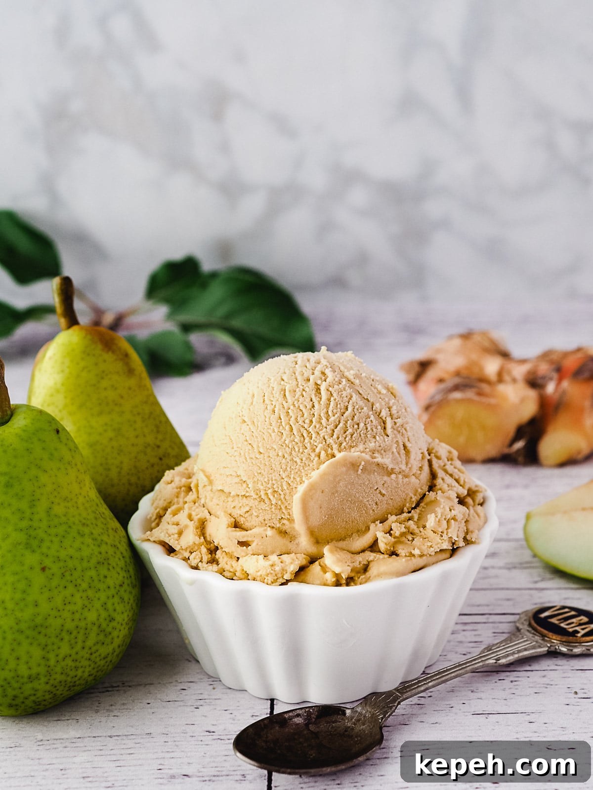 Scoop of pear ice cream with spoon, fresh pears and fresh ginger on the side.