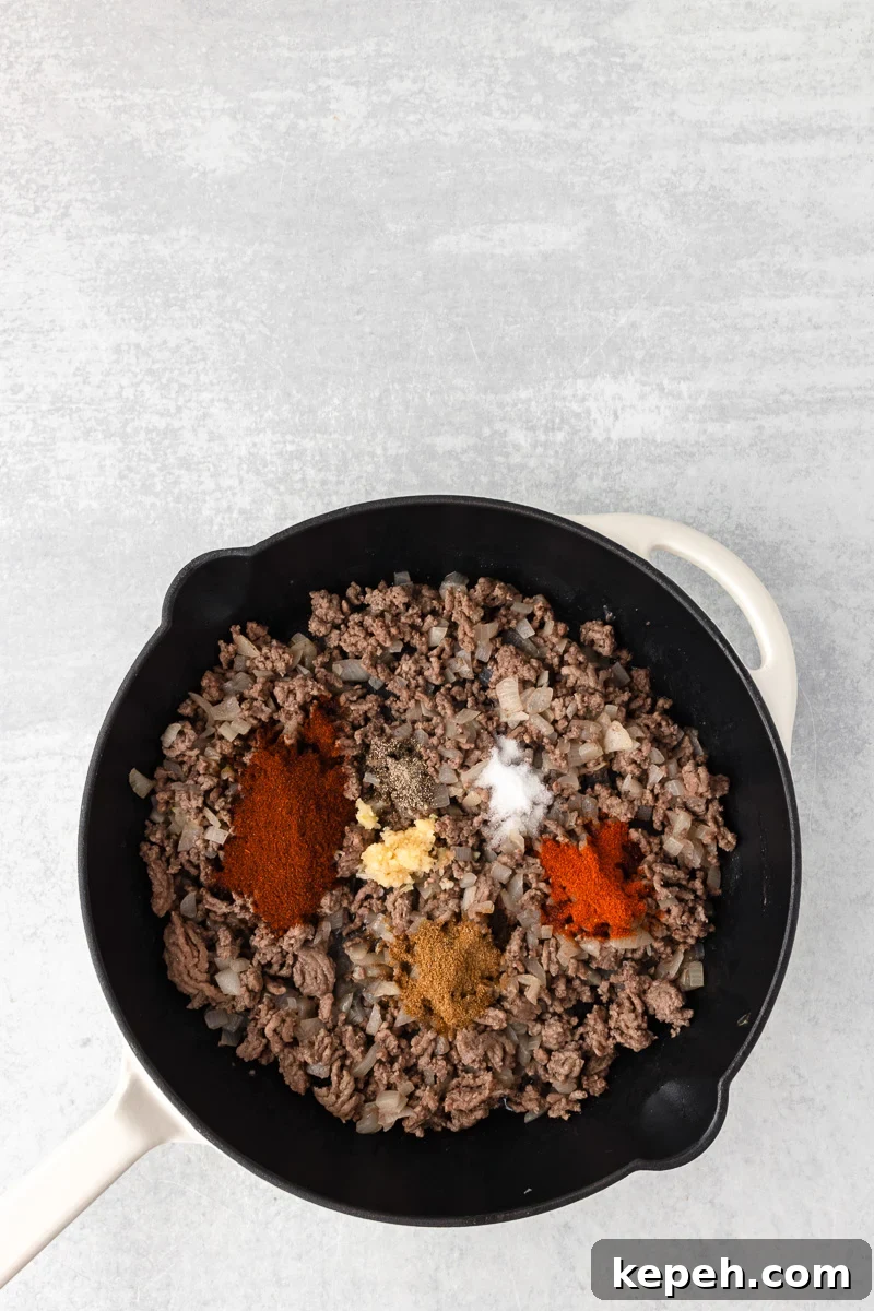 Seasonings are added to the cooked ground beef in the skillet.