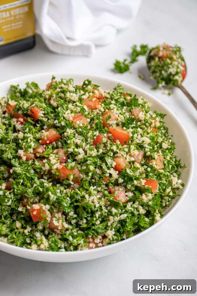 A large white bowl filled with tabbouleh salad with a spoonful out on the side with parsley leaves falling off.