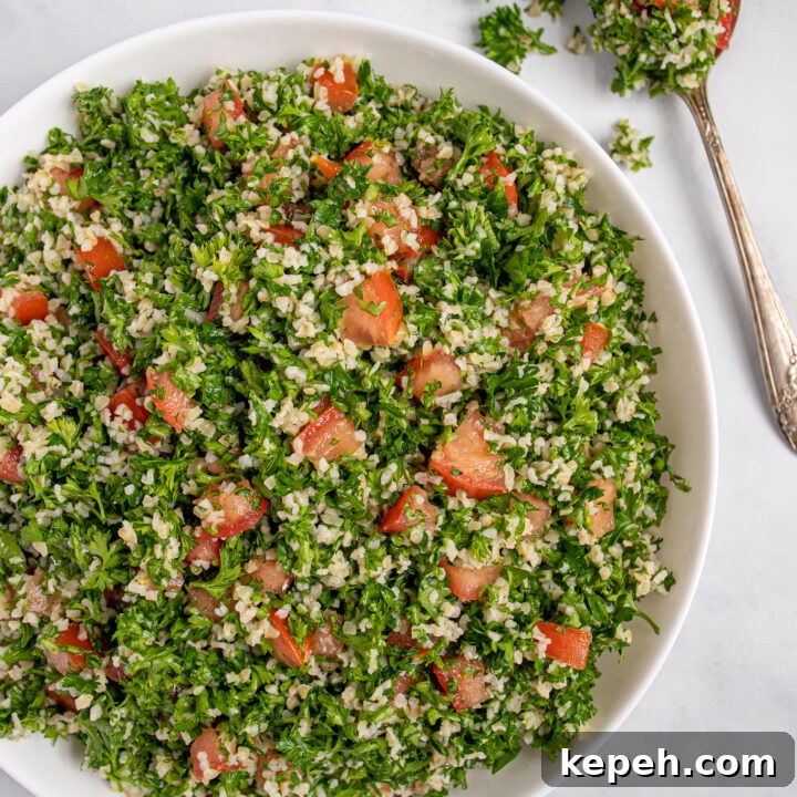 Overhead view of tabbouleh salad in a large white bowl with bright red tomatoes peeking through like jewels.