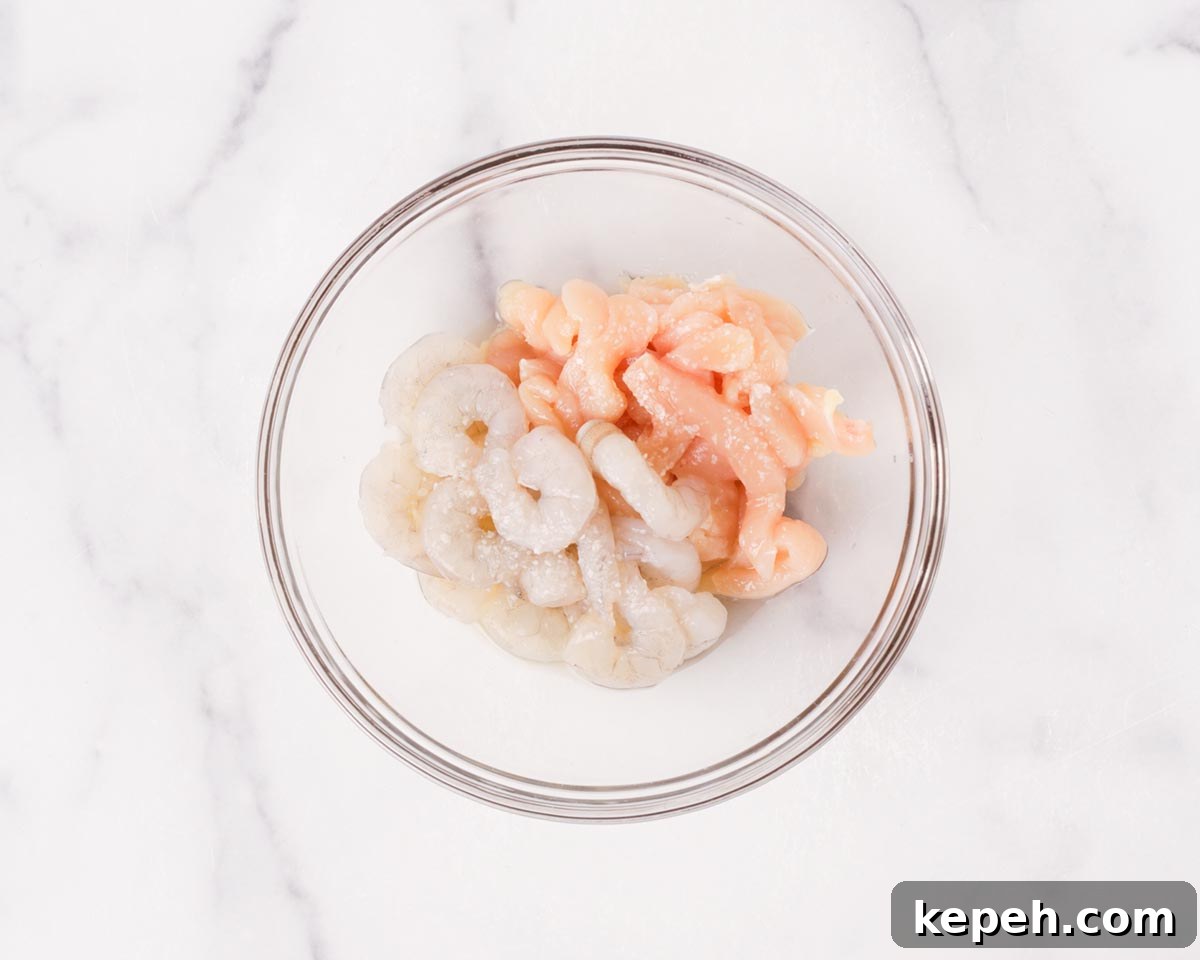 Seasoning shrimps and sliced chicken together.
