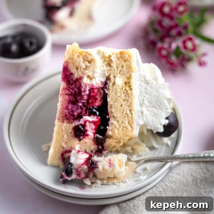 slice of white forest cake on a plate with a fork and flowers and a bowl of cherries in the background