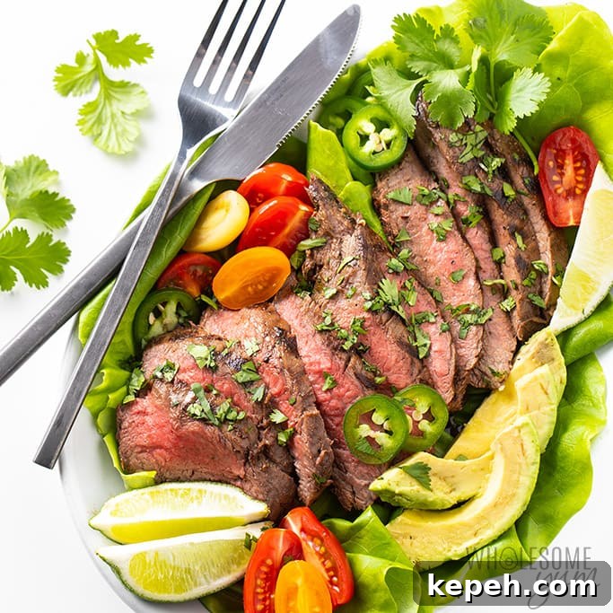 sliced steak on top of butter lettuce leaves with tomatoes and lime slices on the side