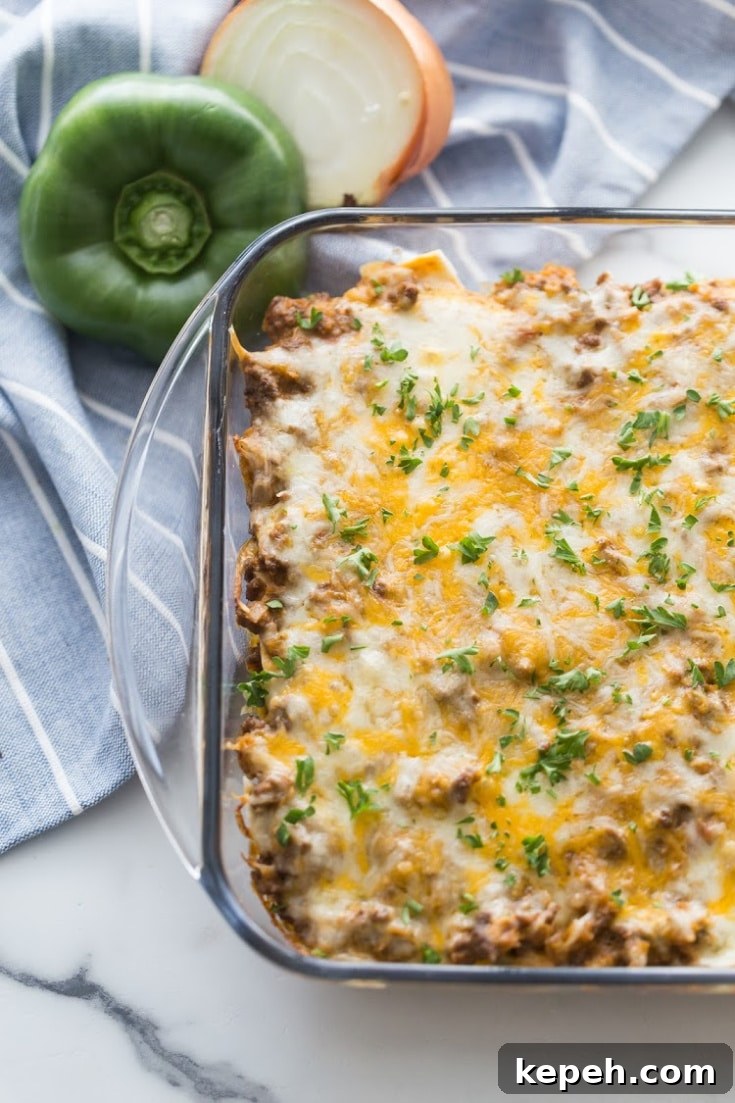 Mexican taco bake in a clear casserole dish with a green pepper and onion on the side