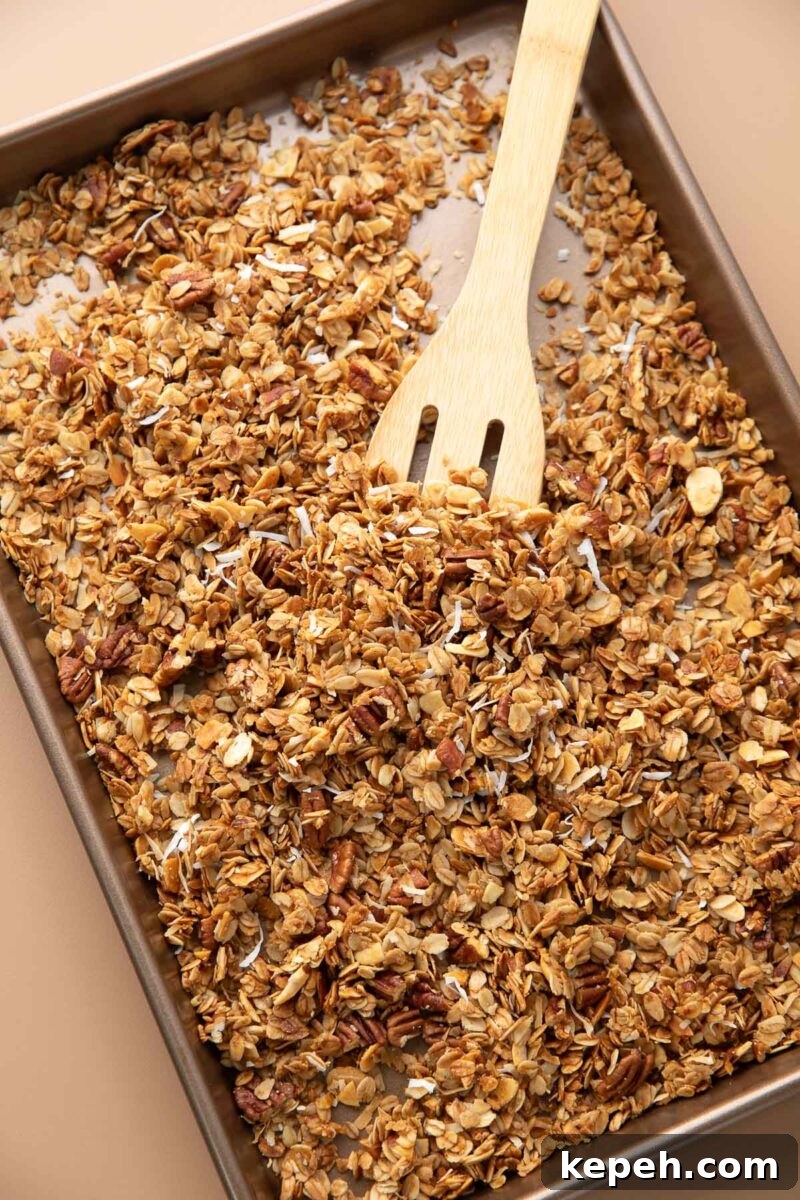 Crunchy Coconut Granola Recipe for Homemade Morning Boost 5 coconut granola mixed with a wooden spoon on a sheet pan