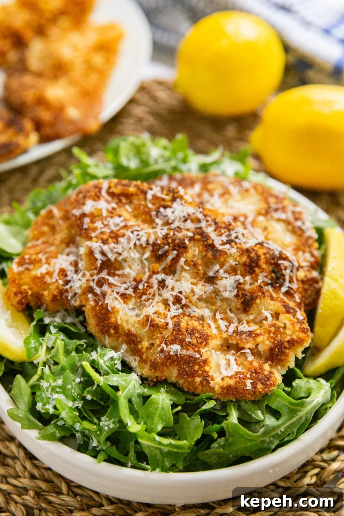 Veal Scallopini with Lemon Butter Sauce Recipe 2 Veal scallopini on a bed of dressed arugula with lemon wedges on a white plate.