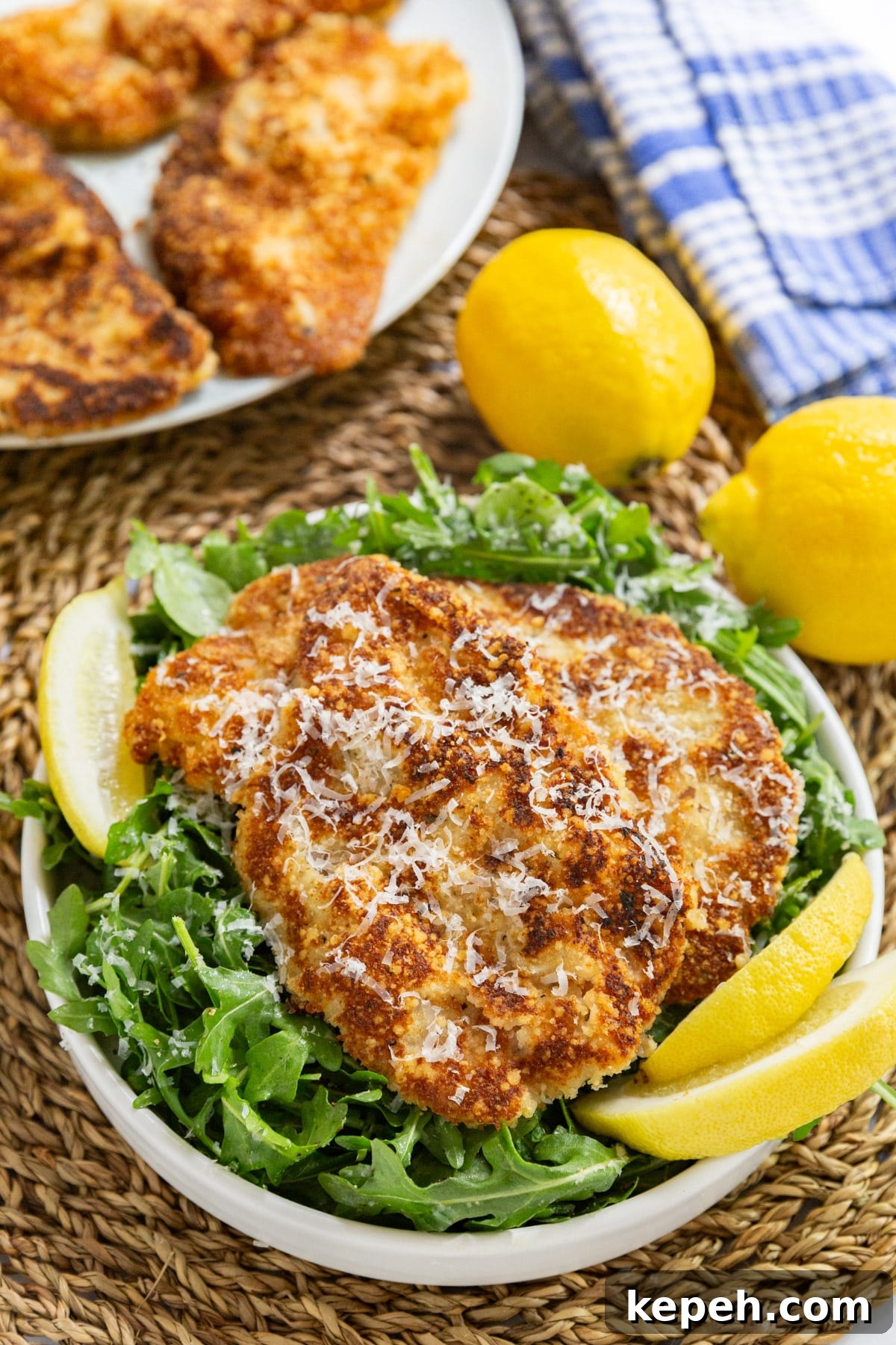 Veal Scallopini with Lemon Butter Sauce Recipe 9 A plate of veal scallopini on a bed of dressed arugula with the rest of the veal on a platter behind it.