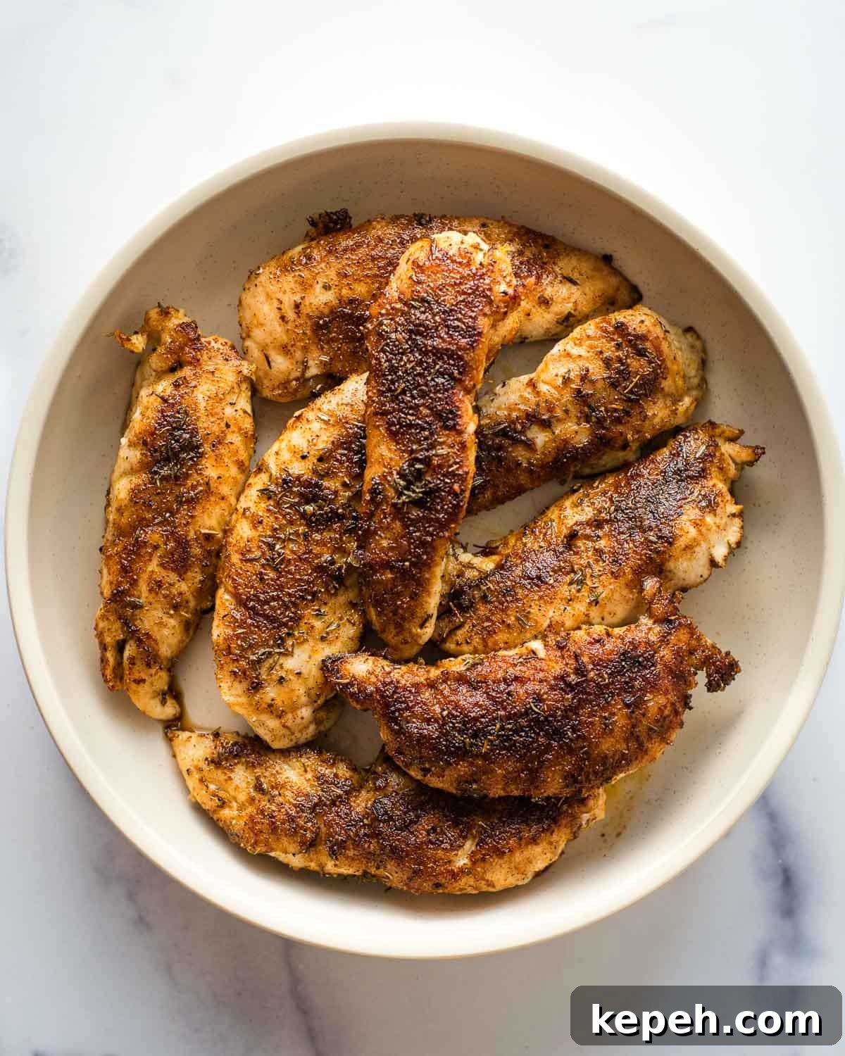 Cajun Blackened Chicken Tenders Recipe with Crispy Pan-Seared Flavor 2 Blackened chicken tenders in a white bowl on a table.