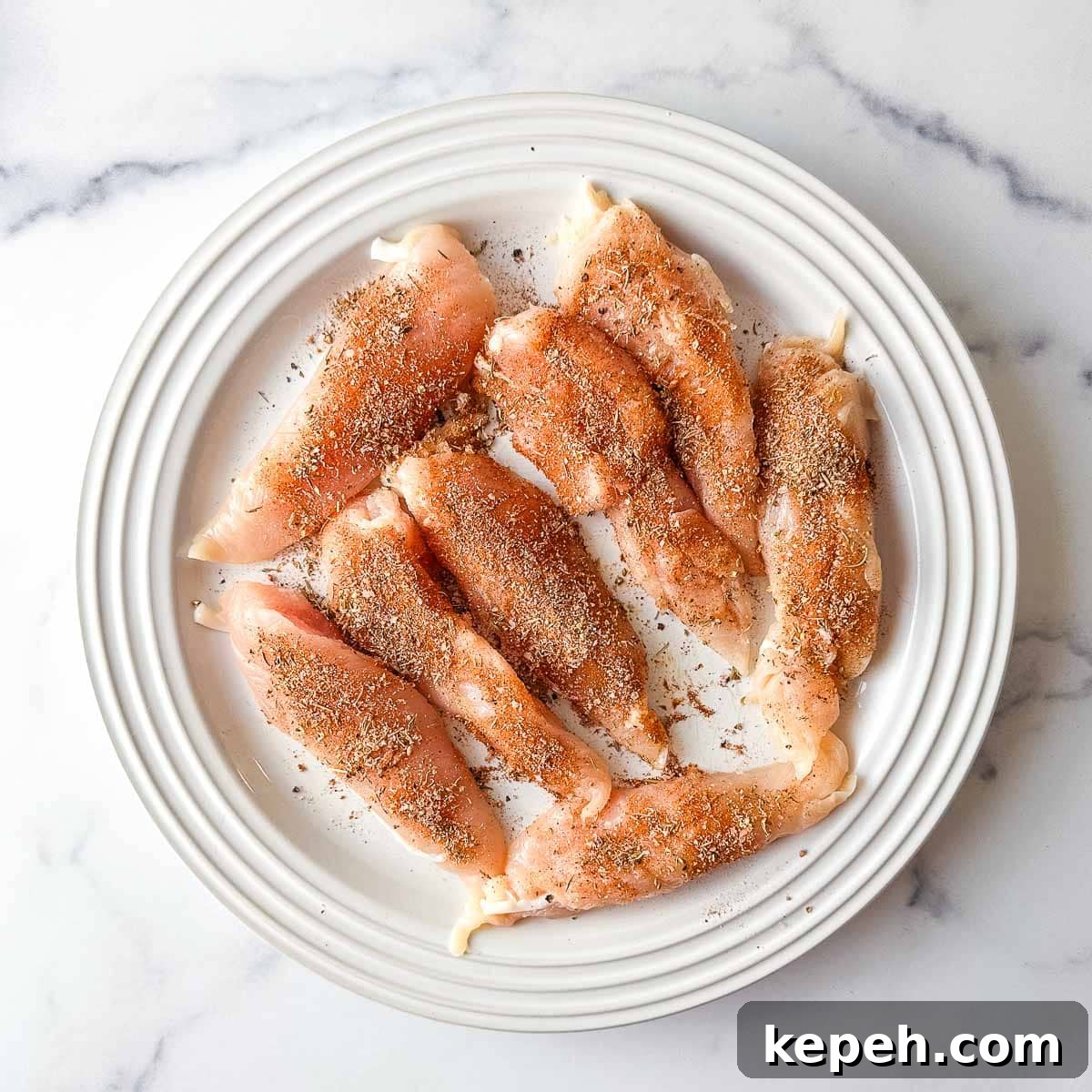 Cajun Blackened Chicken Tenders Recipe with Crispy Pan-Seared Flavor 6 Chicken tenders on a white plate with blackened seasoning.