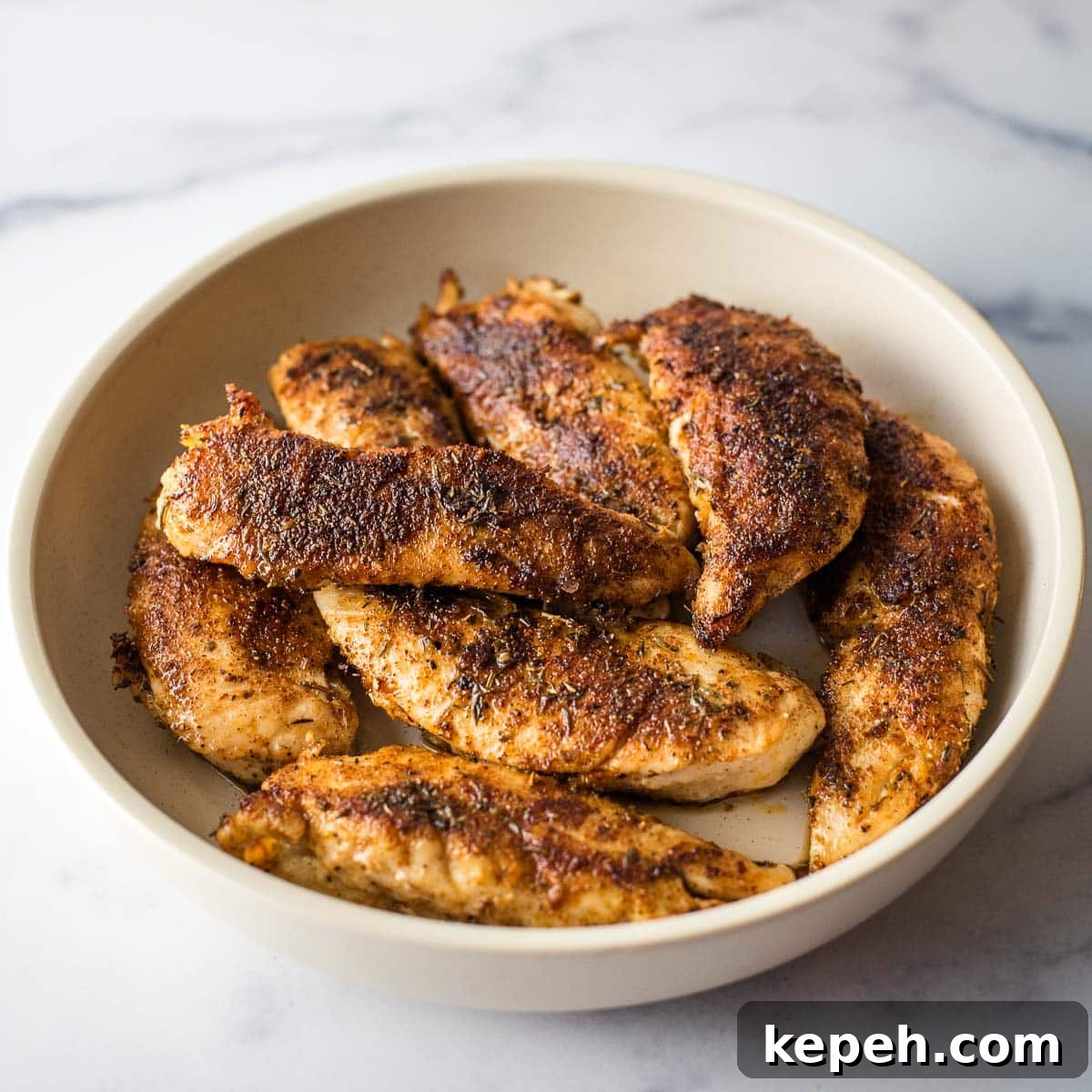 Cajun Blackened Chicken Tenders Recipe with Crispy Pan-Seared Flavor 9 Blackened chicken tenders in a white bowl on a marble table.
