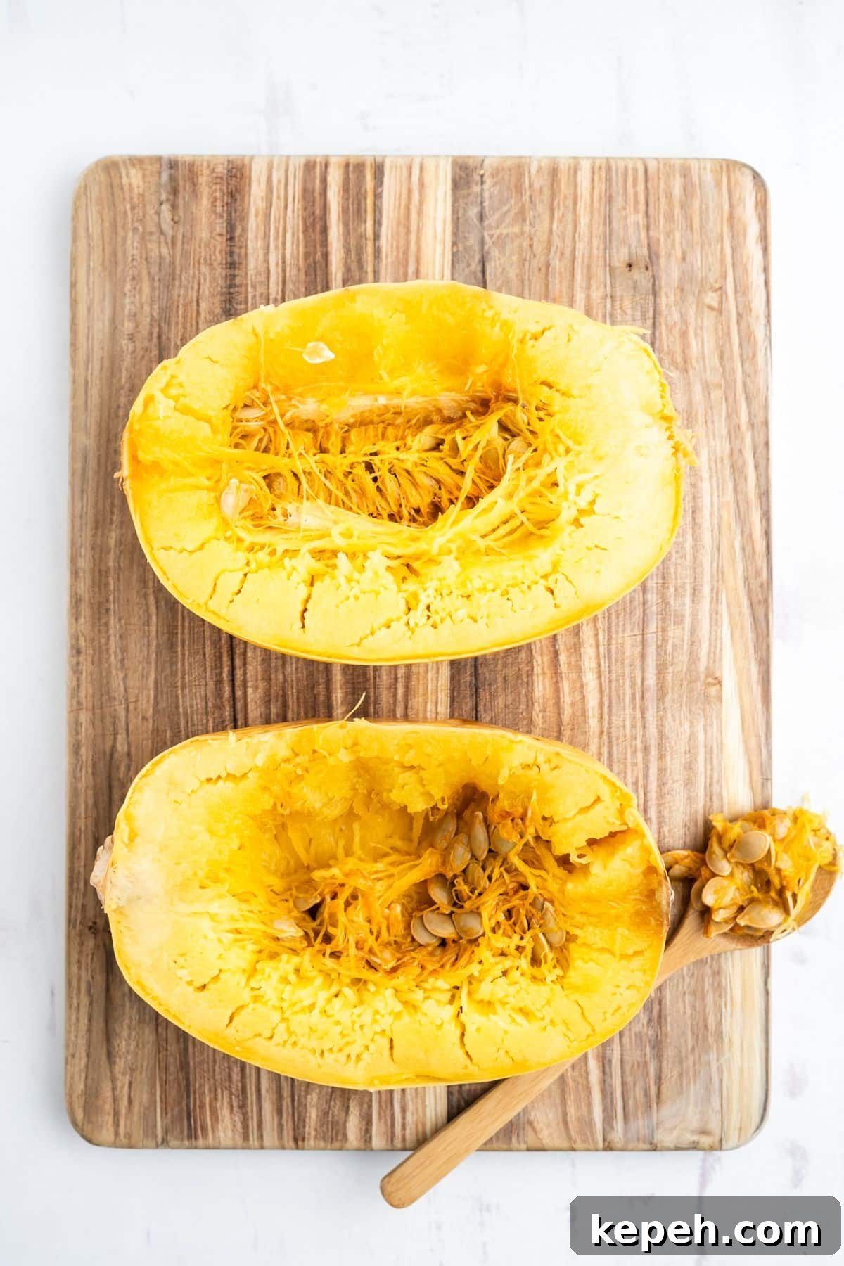 Spaghetti squash laid on a wooden cutting board and a spoon removing the seeds.