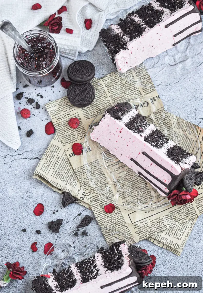 A pink frosted cake with chocolate layers and topped with dark chocolate oreos, raspberries, and bright red flowers.