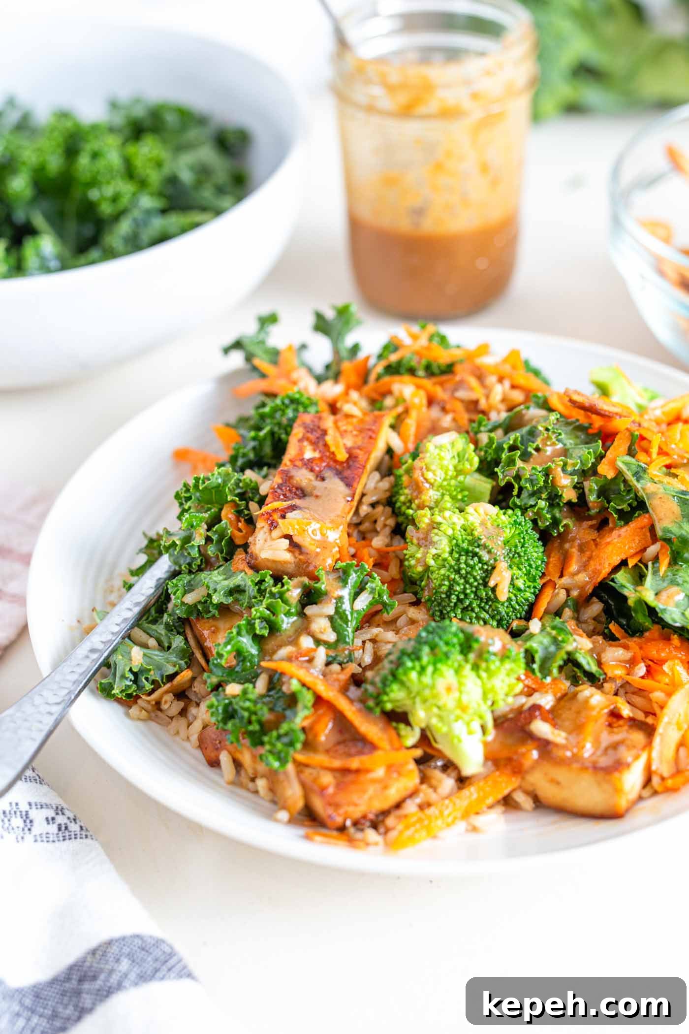 Crispy Tofu and Broccoli Rice Bowl with Sesame-Ginger Sauce 2 A bowl with shredded carrot, broccoli, tofu, kale and a creamy sauce.