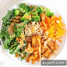 A bowl with tofu, sauce, kale, broccoli, carrot and coconut bacon.