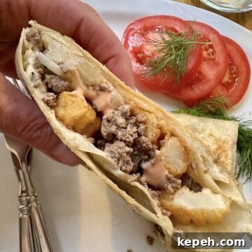 How to Make Authentic French Tacos at Home 17 One half of a French taco held by a hand over a plate with silverware, sliced tomato and dill.