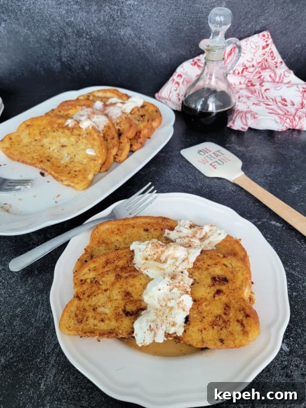 Eggnog French Toast Recipe with Video Tutorial 9 Eggnog French Toast slices on a white plate garnished with eggnog whipped cream and cinnamon/nutmeg next to a platter and a spatula
