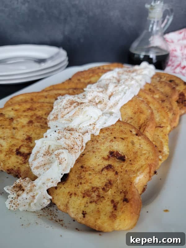 Eggnog French Toast Recipe with Video Tutorial 10 Eggnog French Toast slices on a white plate garnished with eggnog whipped cream and cinnamon/nutmeg