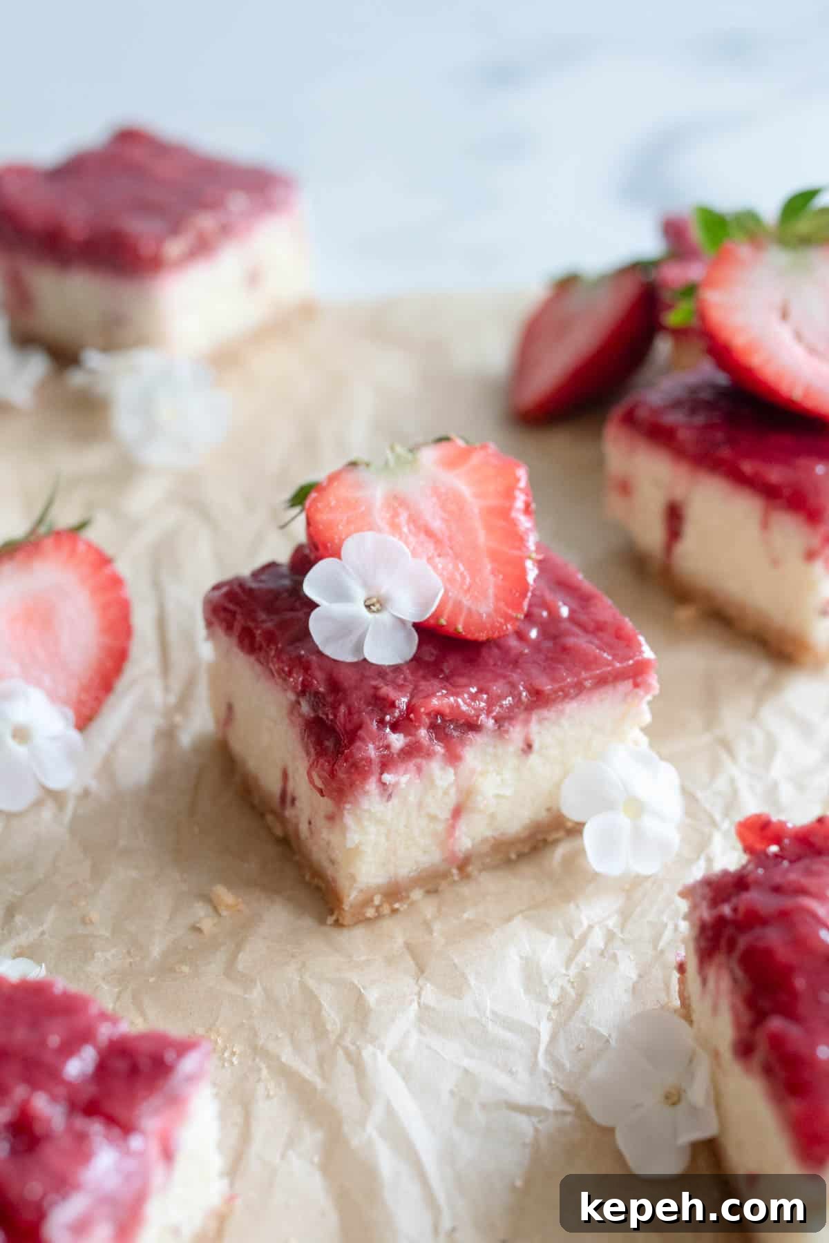 Strawberry Cheesecake Bar Recipe: Creamy No-Bake Dessert Bars 2 A cheesecake bar topped with strawberries and a white flower on top of brown parchment paper.