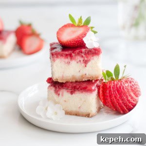 Strawberry Cheesecake Bar Recipe: Creamy No-Bake Dessert Bars 15 Two strawberry cheesecake bars stacked next to two fresh strawberries and little white flours on a white plate.