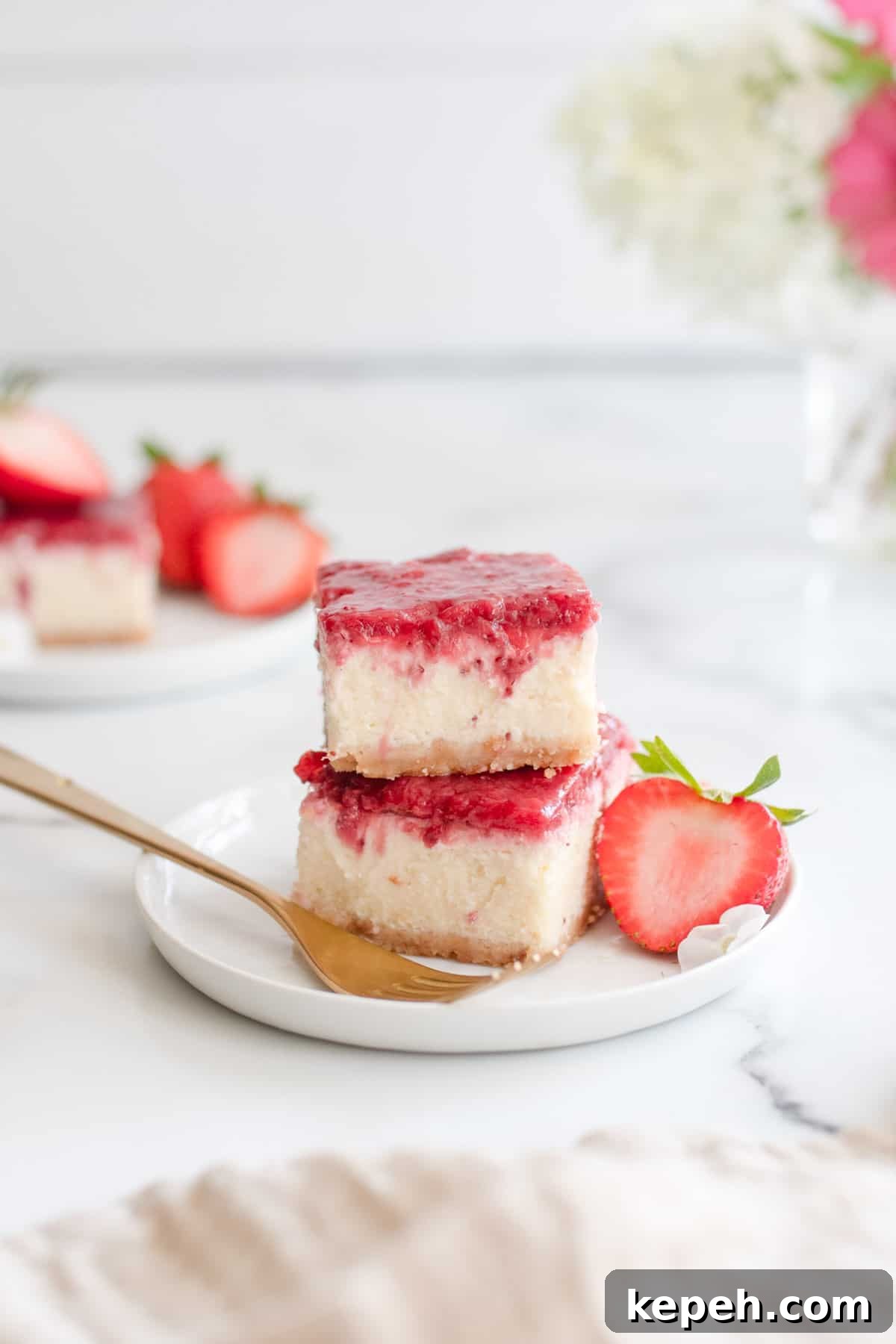 Strawberry Cheesecake Bar Recipe: Creamy No-Bake Dessert Bars 9 Two cheesecake bars stacked and topped with strawberry compote next to a gold fork.