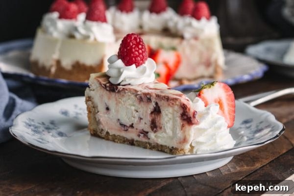 Slice of keto cheesecake with raspberry swirl on a plate with whipped cream and fresh raspberries and strawberries.