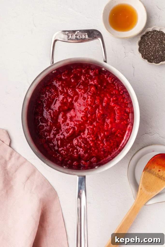 Raspberry Chia Seed Jam Recipe: Quick No-Cook Fruit Spread 3 A saucepan full of cooked down raspberries next to some honey, chia seeds, and a wooden spoon.