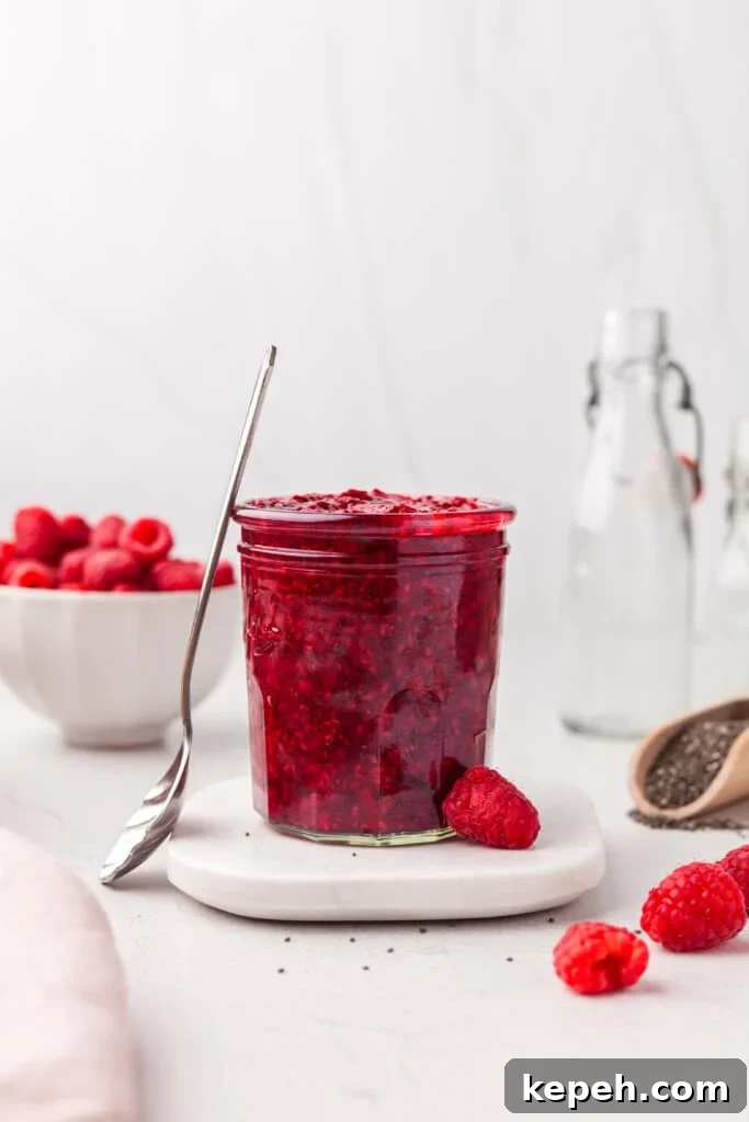 Raspberry Chia Seed Jam Recipe: Quick No-Cook Fruit Spread 5 A jar of homemade raspberry chia jam with a spoon leaning against it.
