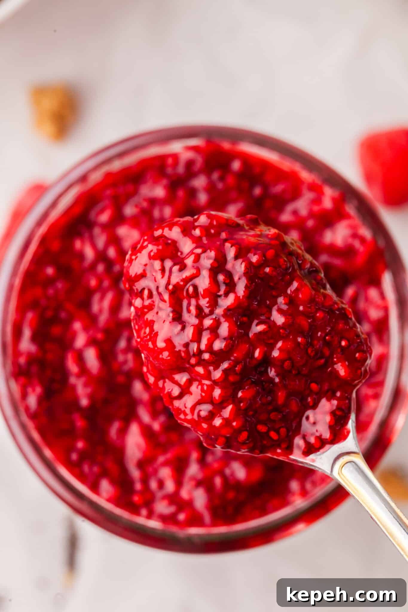 Raspberry Chia Seed Jam Recipe: Quick No-Cook Fruit Spread 6 Overhead image of a spoon lifting some raspberry chia jam out of a jar.