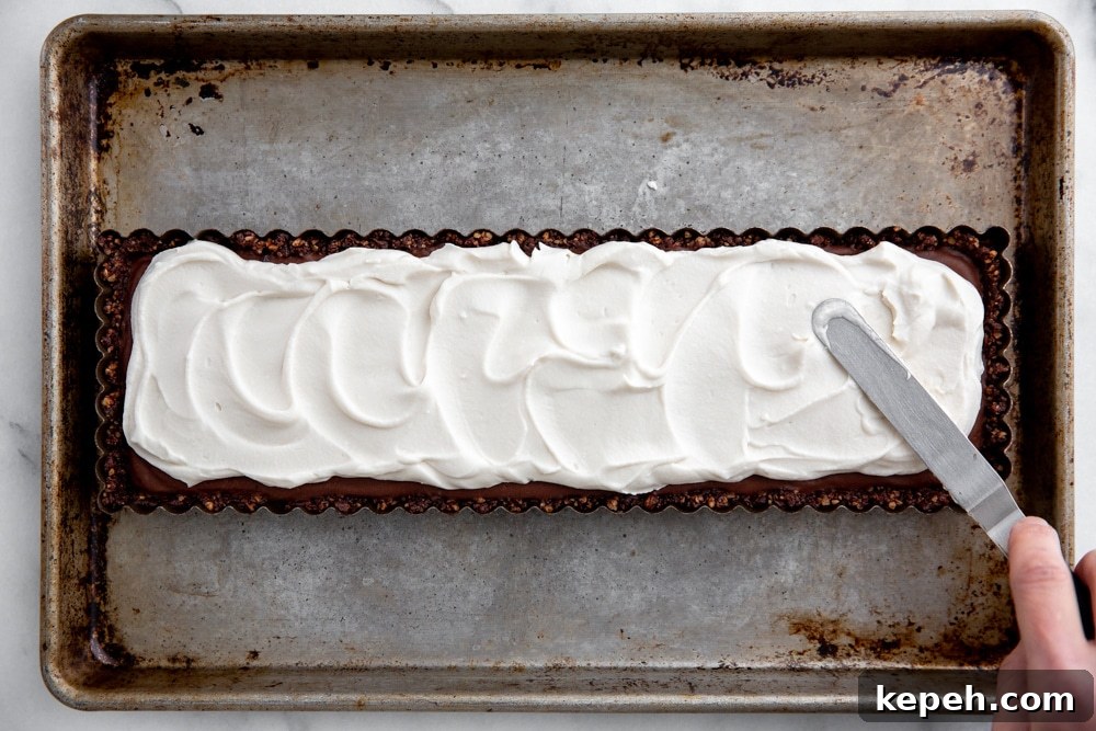 Hand using a small off-set spatula to spread the coconut whipped cream over the vegan chocolate tart.