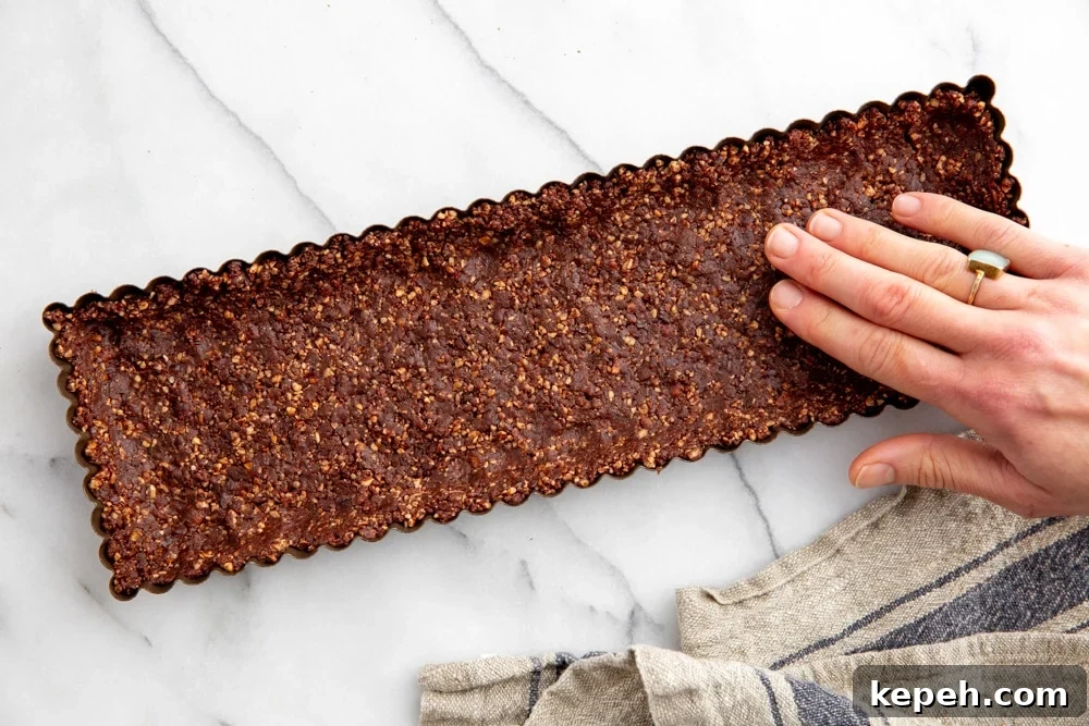 Hand pressing the date nut crust into a tart pan.