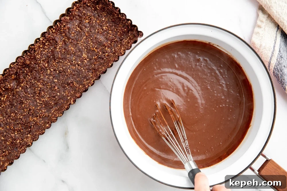 Hand whisking chocolate pudding in a saucepan with the date nut crust alongside.