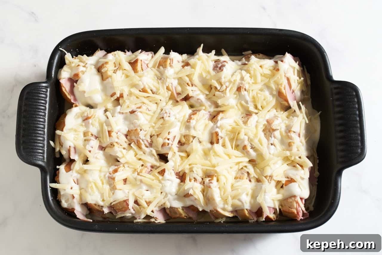 Stacked baguette slices in a black casserole dish layered with ham slices and topped with bechamel sauce and gruyère cheese.
