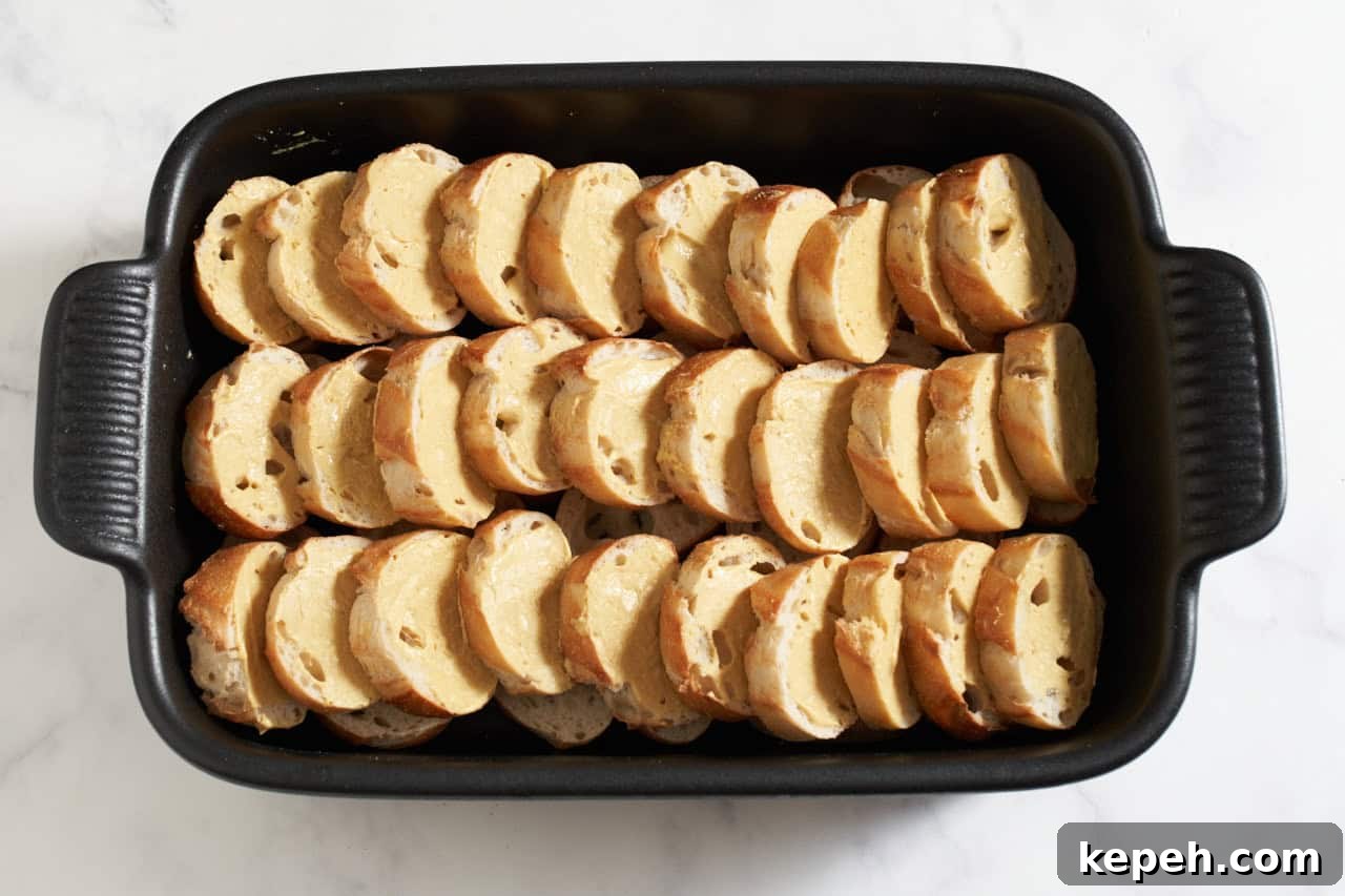 Stacked baguette slices in a black casserole dish topped with dijon mustard.