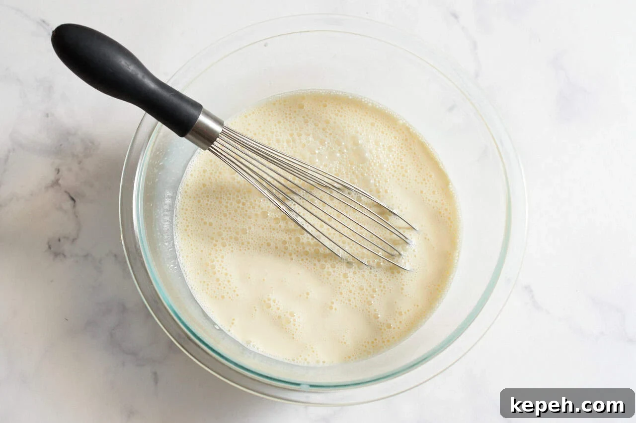 Eggs and half and half whisked together in a glass bowl.