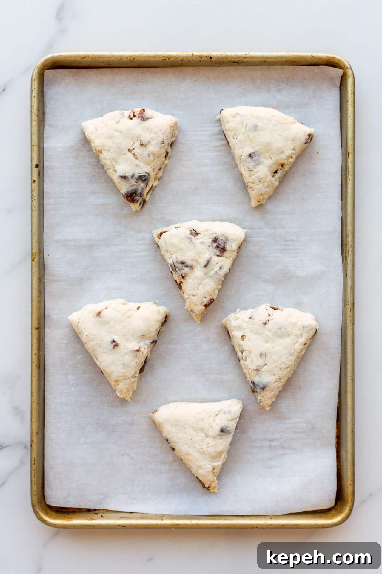 Chewy Date Scones with Honey Glaze 5 Six (6) triangle wedge scones on a parchment-lined sheet pan before baking