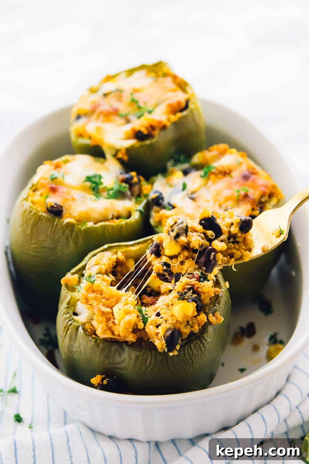Four quinoa stuffed peppers in a white baking dish.