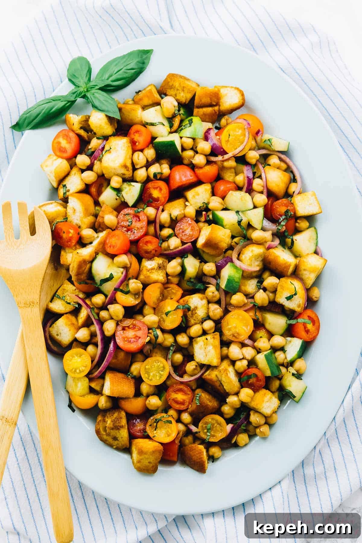 Overhead view of chickpea panzanella salad on a long white plate with a salad fork on the side. 