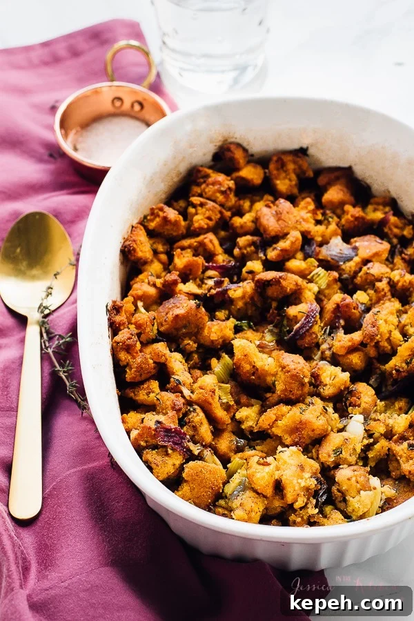 Gluten free cornbread stuffing in a white baking dish with a gold spoon on the side. 