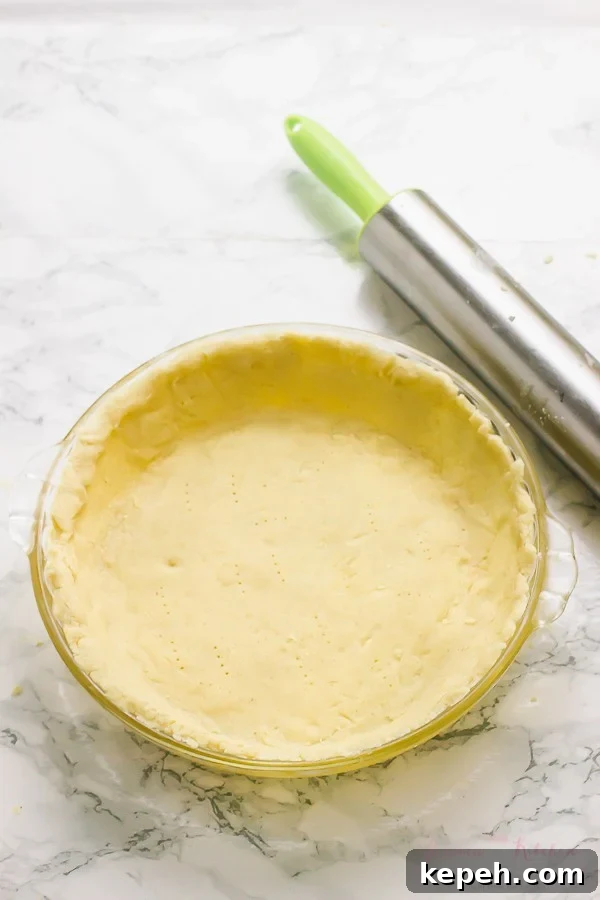 Gluten free pie crust in a glass pie dish with a rolling pin on the side. 