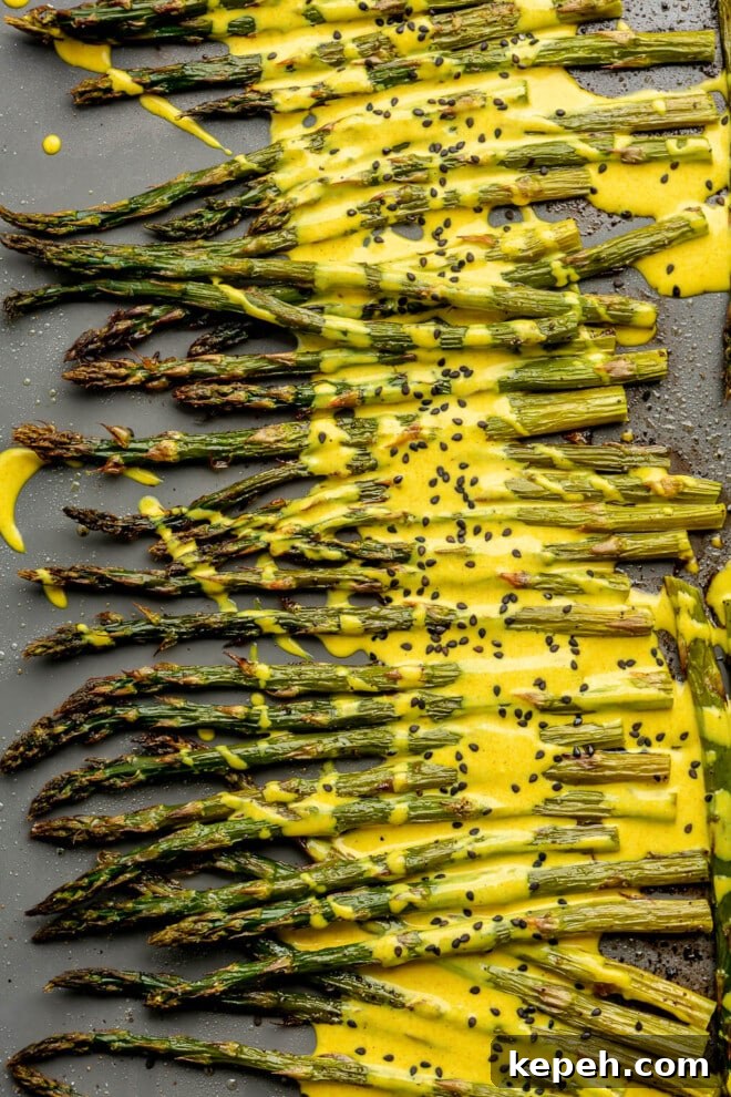 Roasted Asparagus with Lemon Cardamom Cream Sauce 2 A close up of roasted asparagus topped with a bright yellow lemon cardamom sauce and black sesame seeds.
