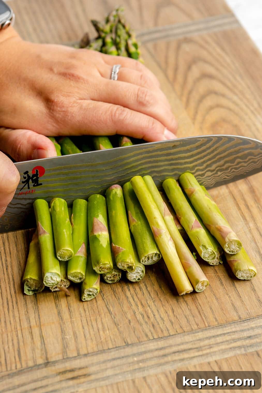 Roasted Asparagus with Lemon Cardamom Cream Sauce 4 A person using a large, sharp knife to cut the ends off of asparagus on a wooden cutting board.