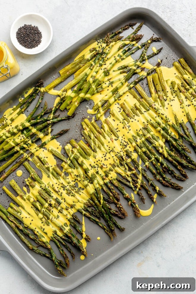Roasted Asparagus with Lemon Cardamom Cream Sauce 10 Roasted asparagus on a sheet pan topped with a bright yellow lemon cardamom sauce and black sesame seeds.