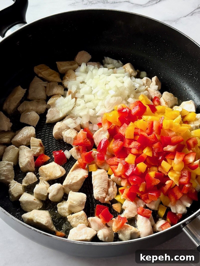 One-Pot Jambalaya Pasta Recipe: Quick Cajun-Style Meal 5 Cooked chicken pieces with peppers and onions in a large skillet.