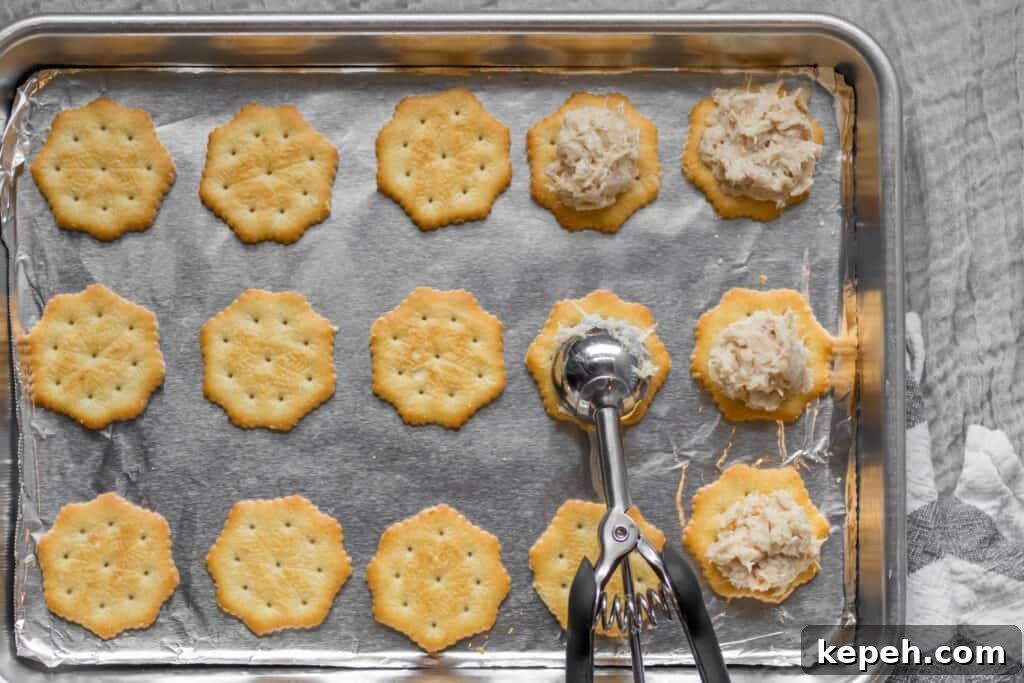 Crispy Cracker Tuna Melts: Quick Tuna Melt Bites 4 crackers on a sheet pan with tuna being scooped on top with cookie scoop