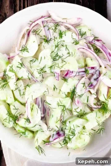 Creamy cucumber and onion salad in a white serving bowl.