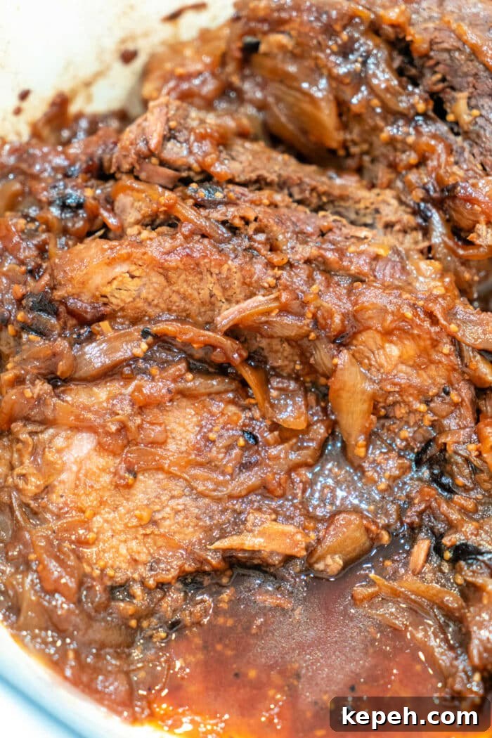 A close-up of braised beef brisket with caramelized onions in a rich, savory roast sauce.