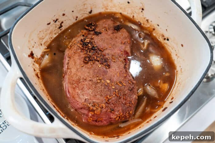 Savory roast beef simmered gently in a pot with caramelized onions and hearty broth on the stove.