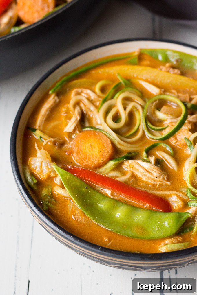 zoomed in shot of chicken curry zoodle bowl with pan in the upper right background and a dark gray napkin in the upper right background