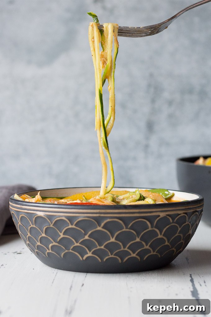 side view of zucchini noodles being lifted out of a bowl of chicken curry zoodles with a fork