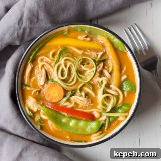top down shot of chicken curry zoodle bowl on a light background with a dark gray napkin to the left and a silver fork to the right